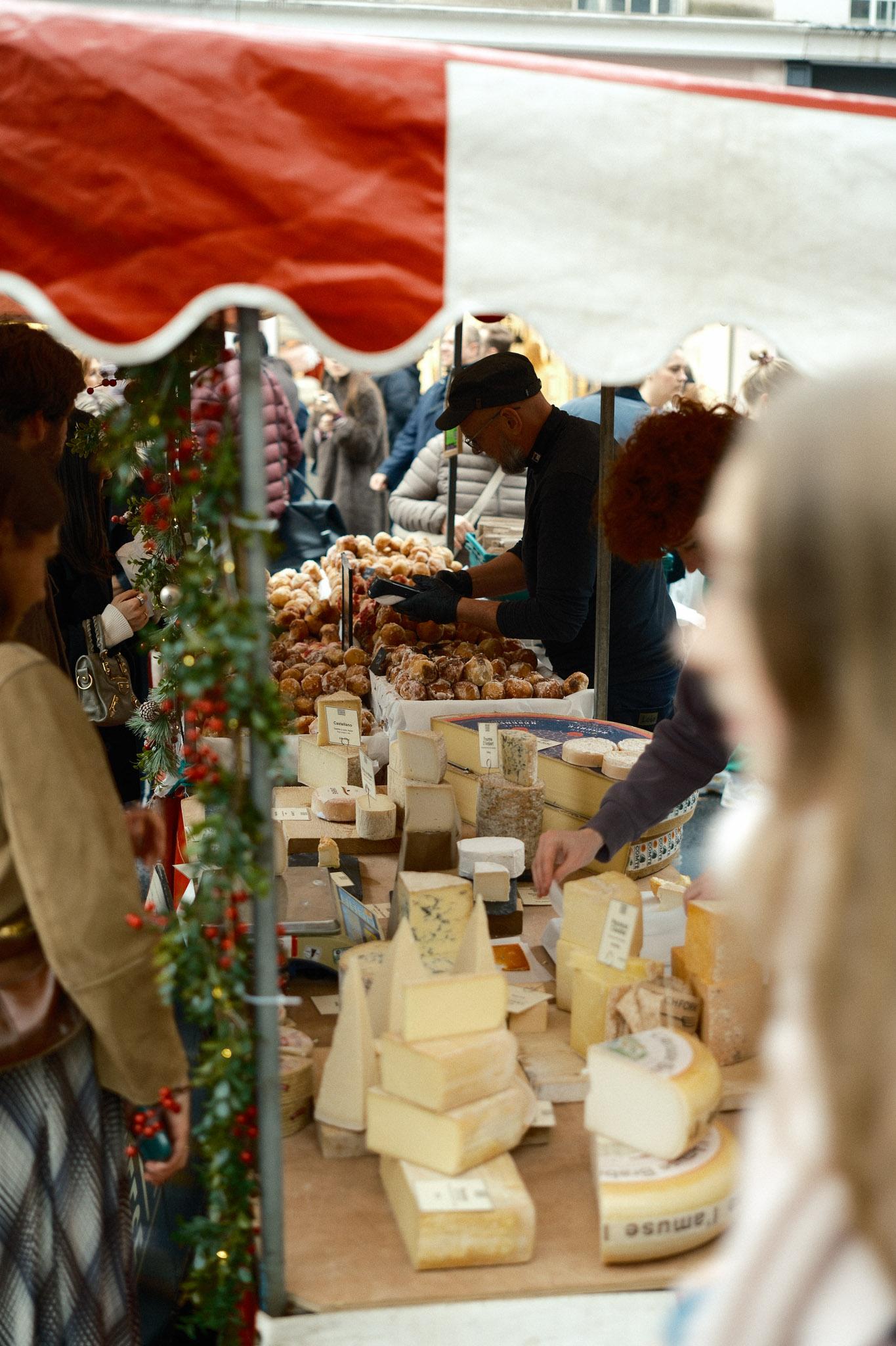 festive market stall offering cheese & donuts with people serving customers