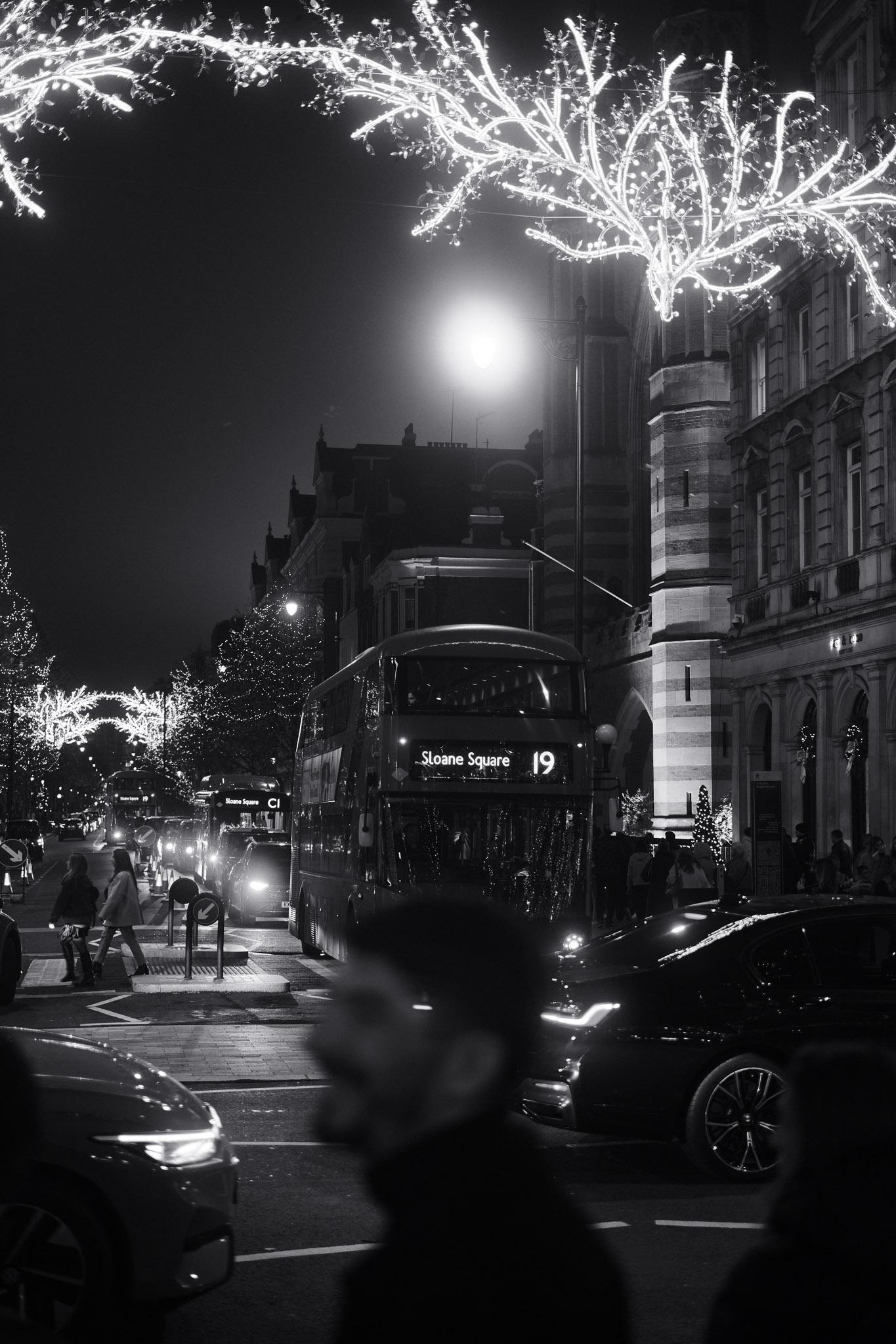 double decker London bus, in the nighttime street, surrounded by Christmas lights