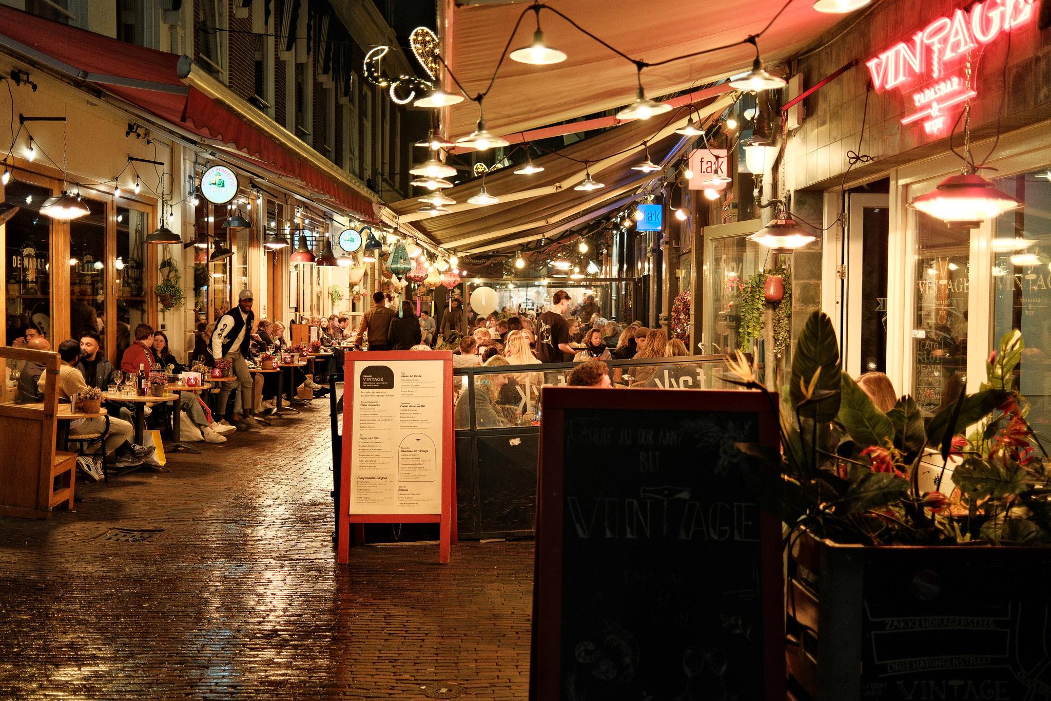 small, yet bustling side street with bars and restaurants, lit up at nighttime in Utrecht